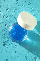 Photo of Open jar of cosmetic product on wet turquoise background, top view