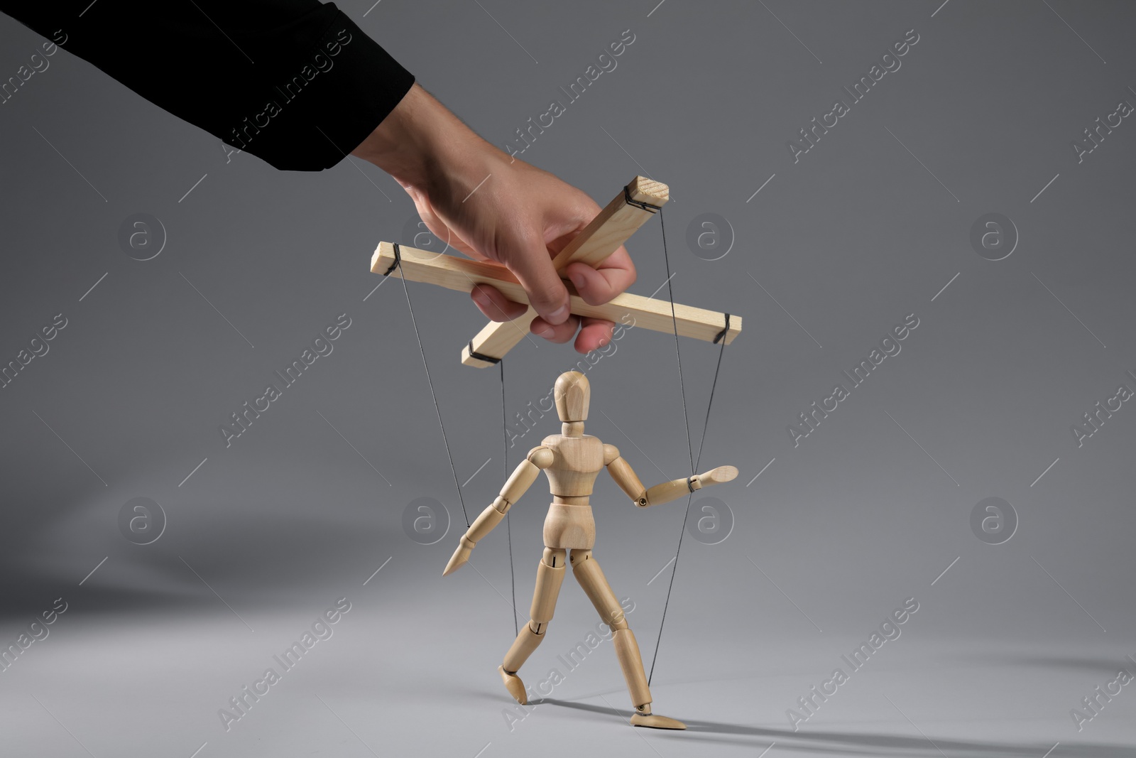 Photo of Man pulling strings of puppet on gray background, closeup