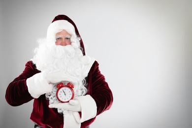 Photo of Santa Claus holding alarm clock on light grey background, space for text. Christmas countdown