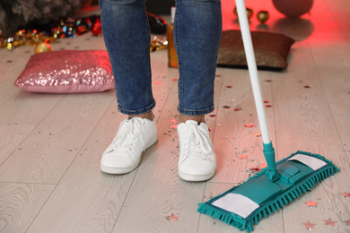 Photo of Man with mop cleaning messy room after New Year party, closeup of legs