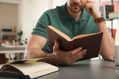 Photo of Man reading book at table in library, closeup