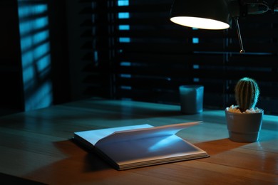 Open book and cactus on wooden table at night