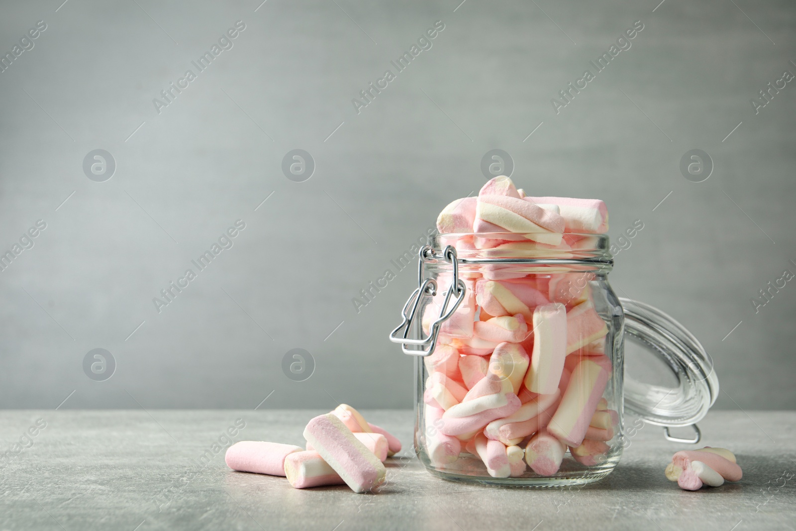 Photo of Glass jar with tasty marshmallows on light grey table. Space for text