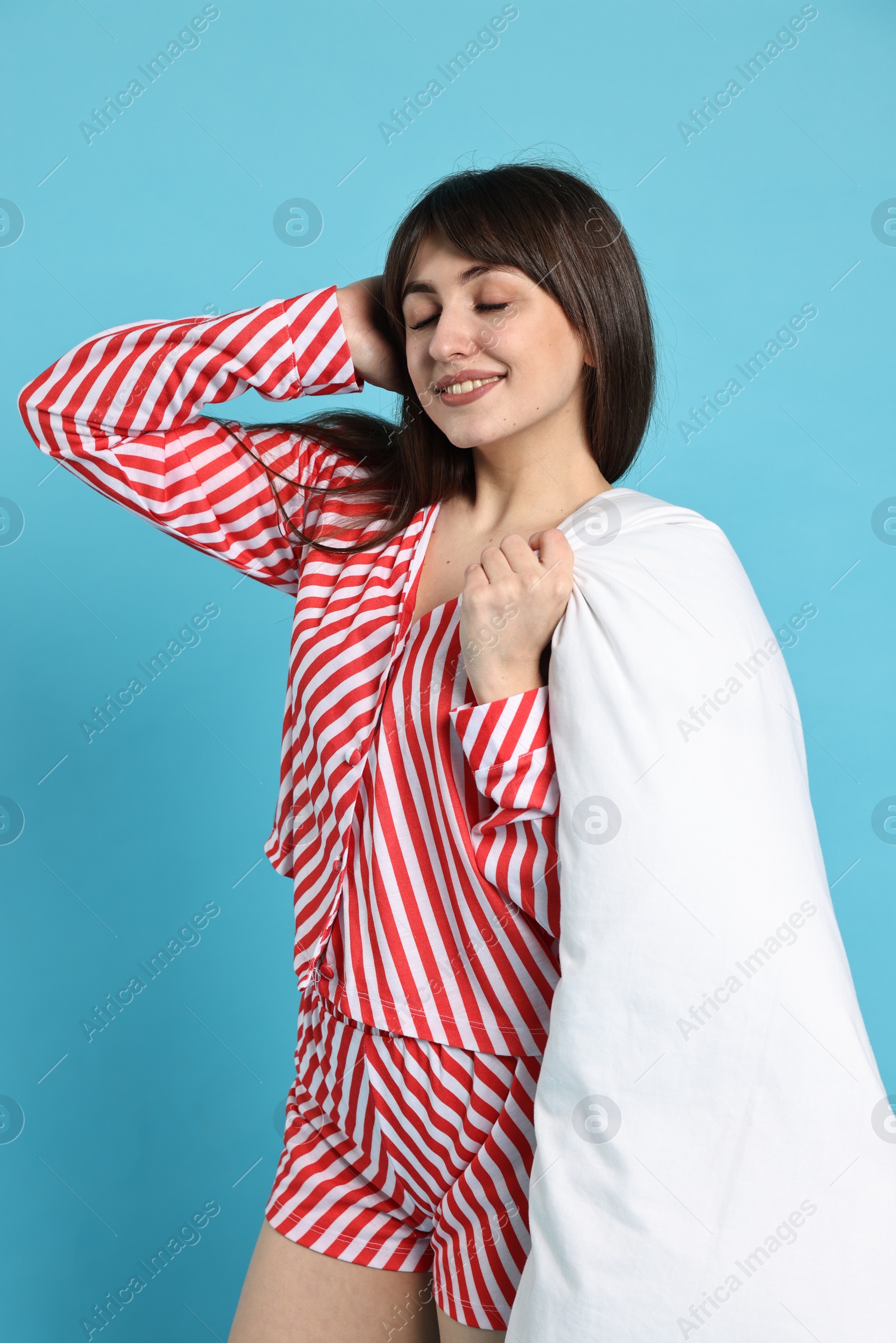 Photo of Happy woman wearing pyjama and holding blanket on light blue background