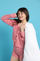 Photo of Happy woman wearing pyjama and holding blanket on light blue background