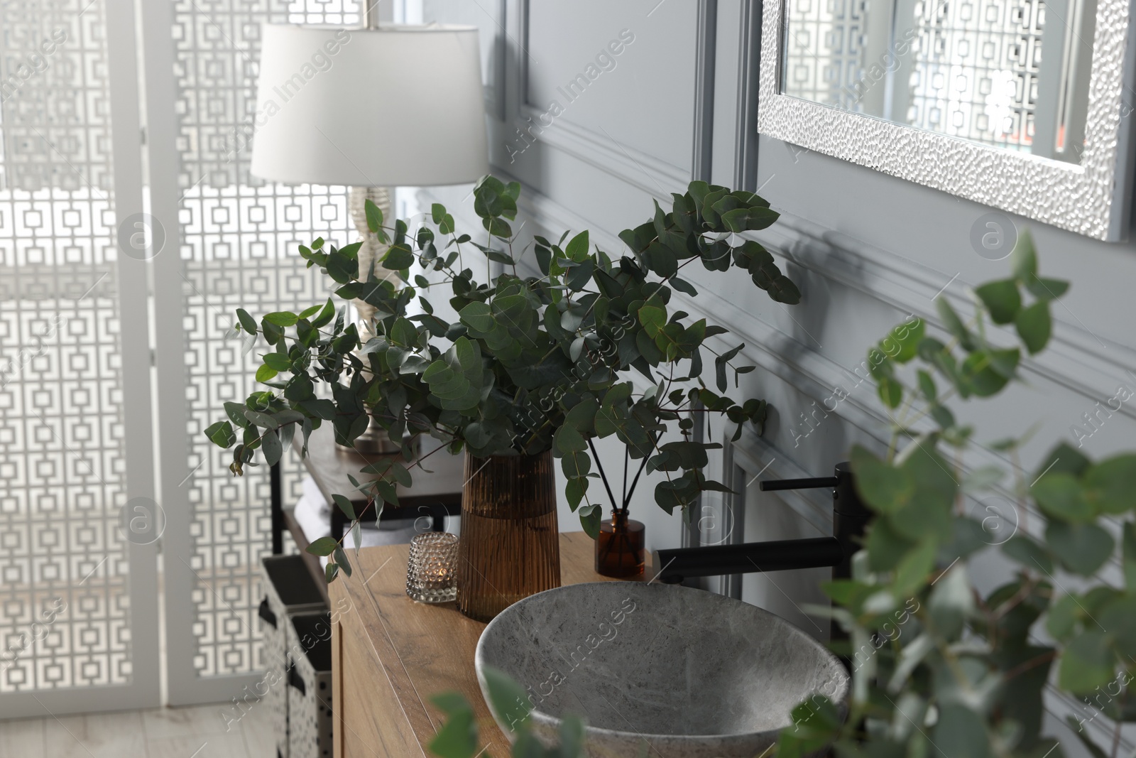 Photo of Eucalyptus branches near vessel sink on bathroom vanity. Interior design