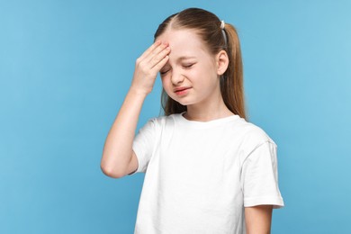 Photo of Little girl suffering from headache on light blue background