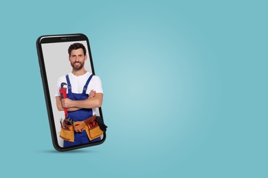 Image of Plumber looking out of smartphone on light blue background. Space for text