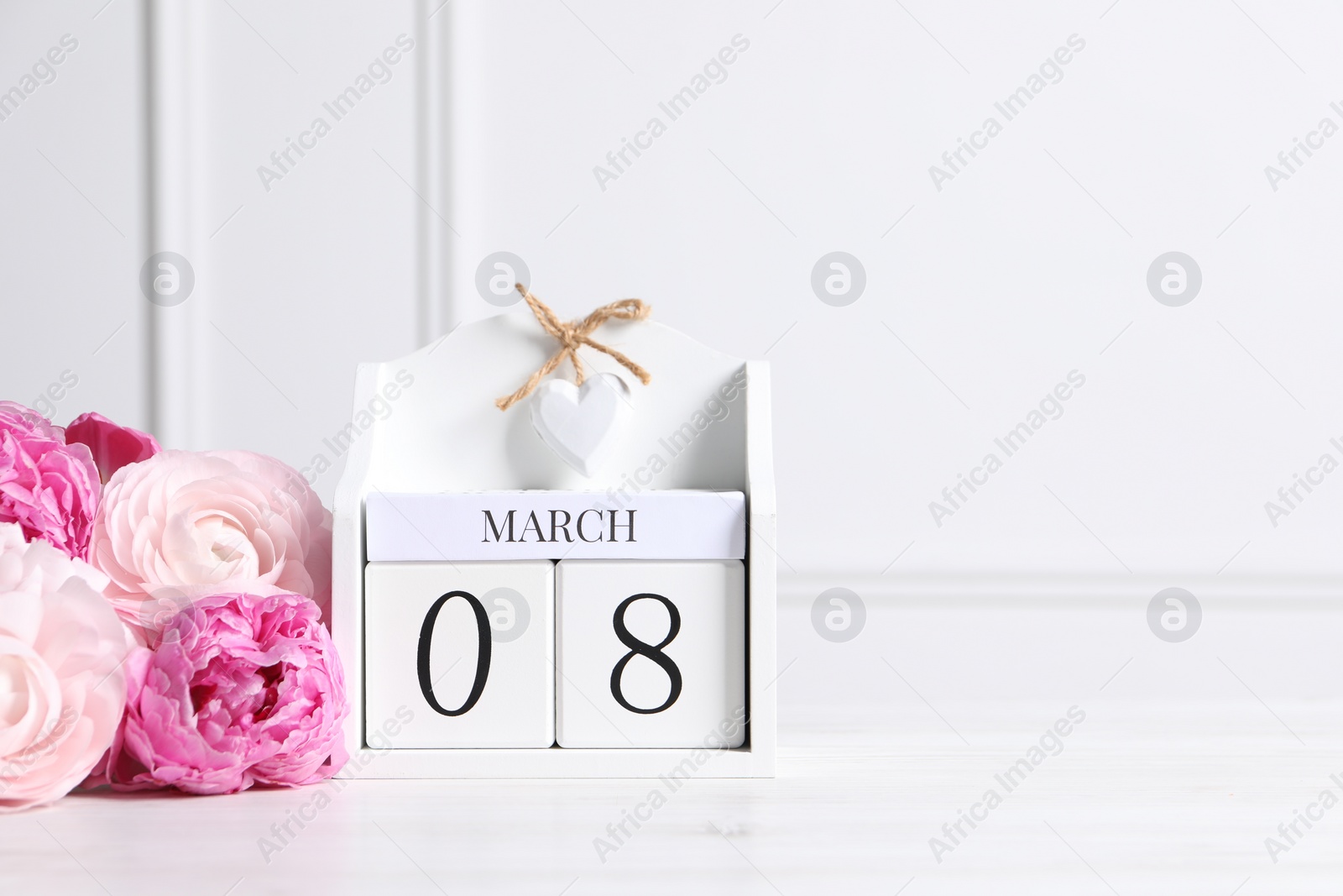 Photo of International Women's day - 8th of March. Wooden block calendar and beautiful flowers on white table, space for text