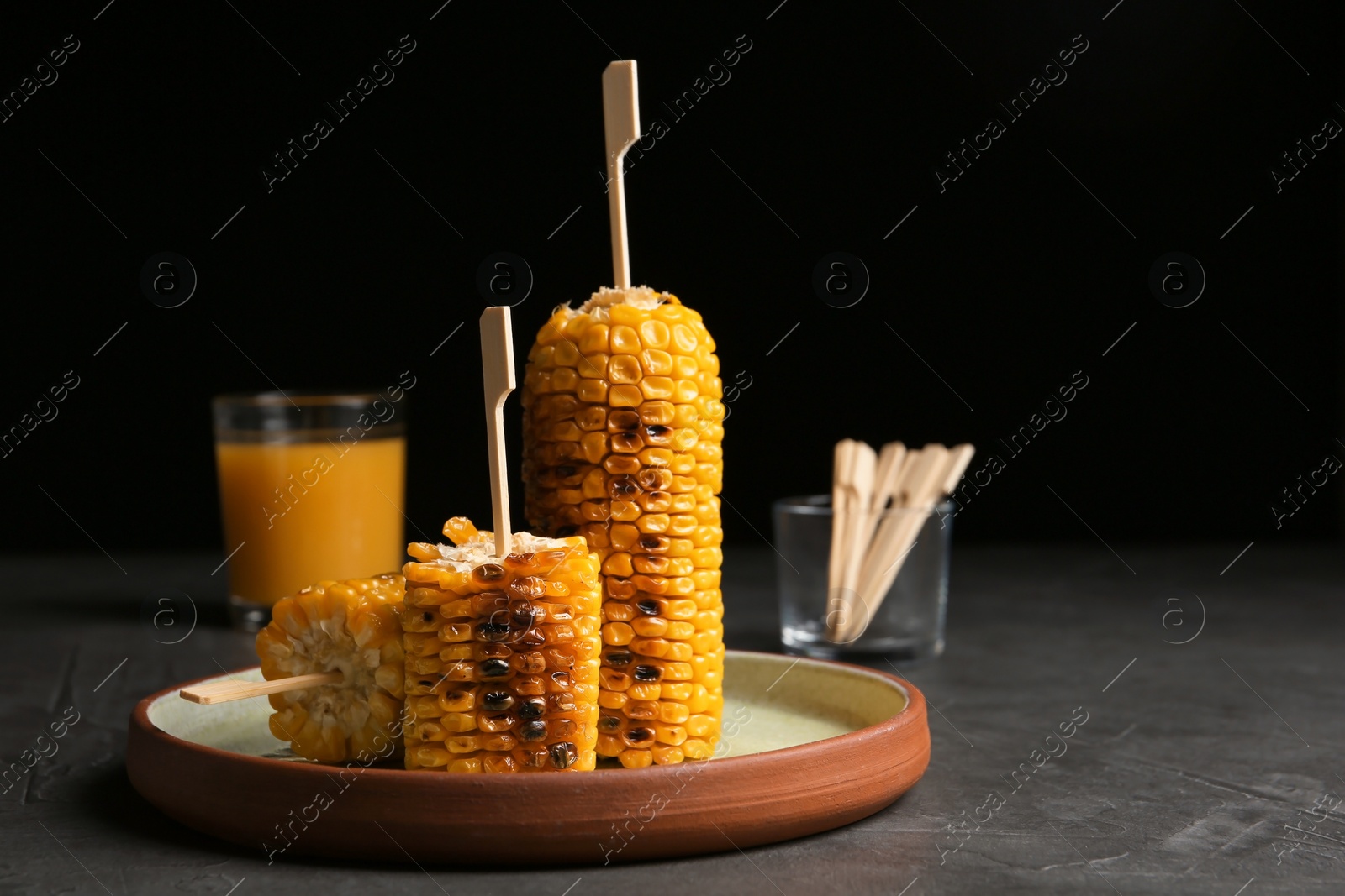 Photo of Plate with delicious grilled corn cobs on gray table against black background