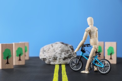 Photo of Overcoming barries for development and success. Wooden human figure with toy bicycle can't move forward due to stone blocking way