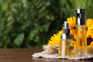 Spray bottles with cooking oil near sunflower seeds and flowers on wooden table against blurred green background. Space for text