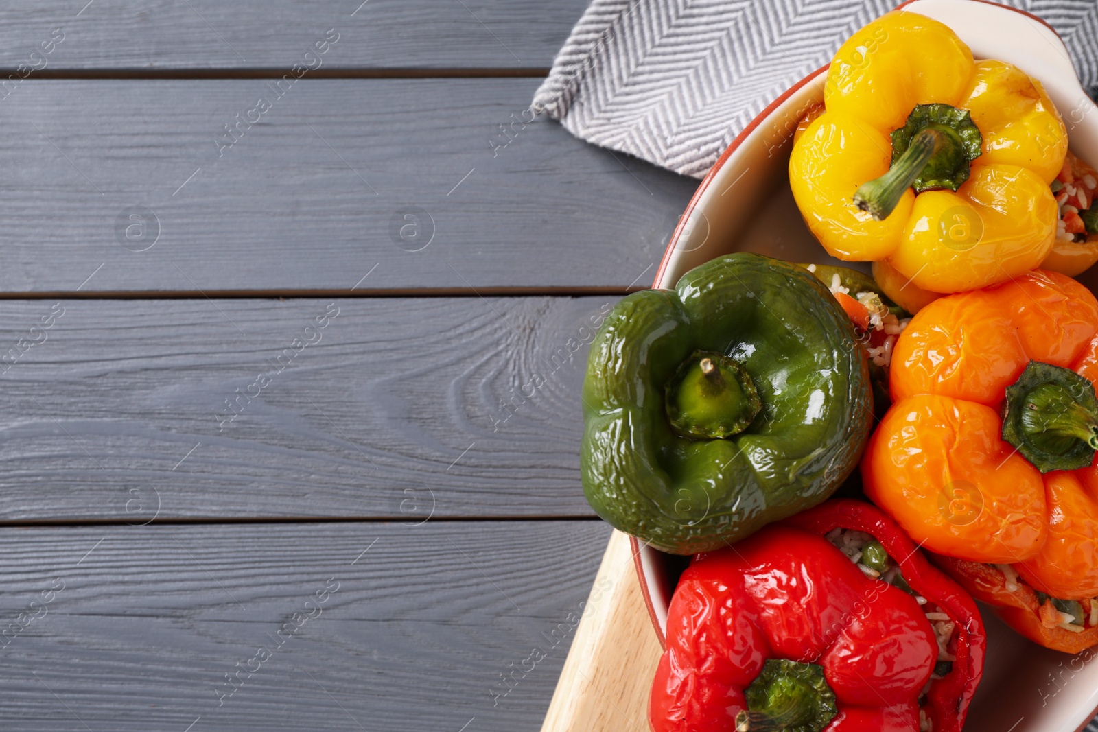 Photo of Tasty stuffed bell peppers in baking dish on grey wooden table, top view. Space for text