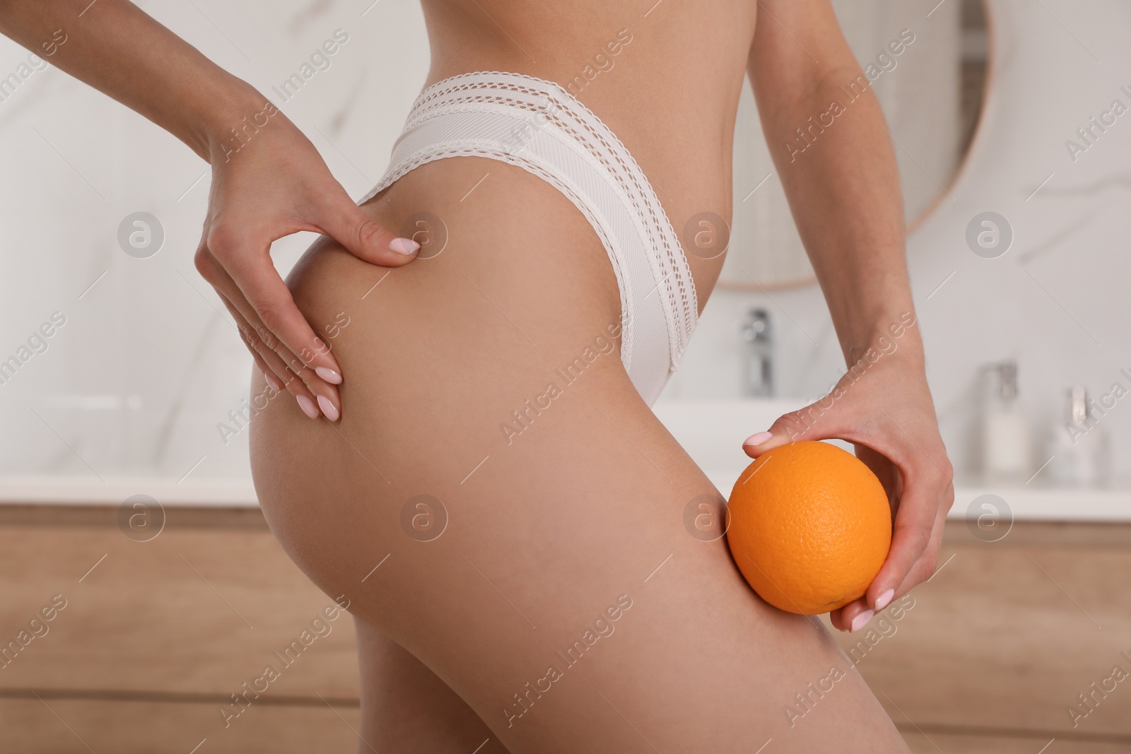 Photo of Closeup view of slim woman in underwear with orange at home. Cellulite problem concept