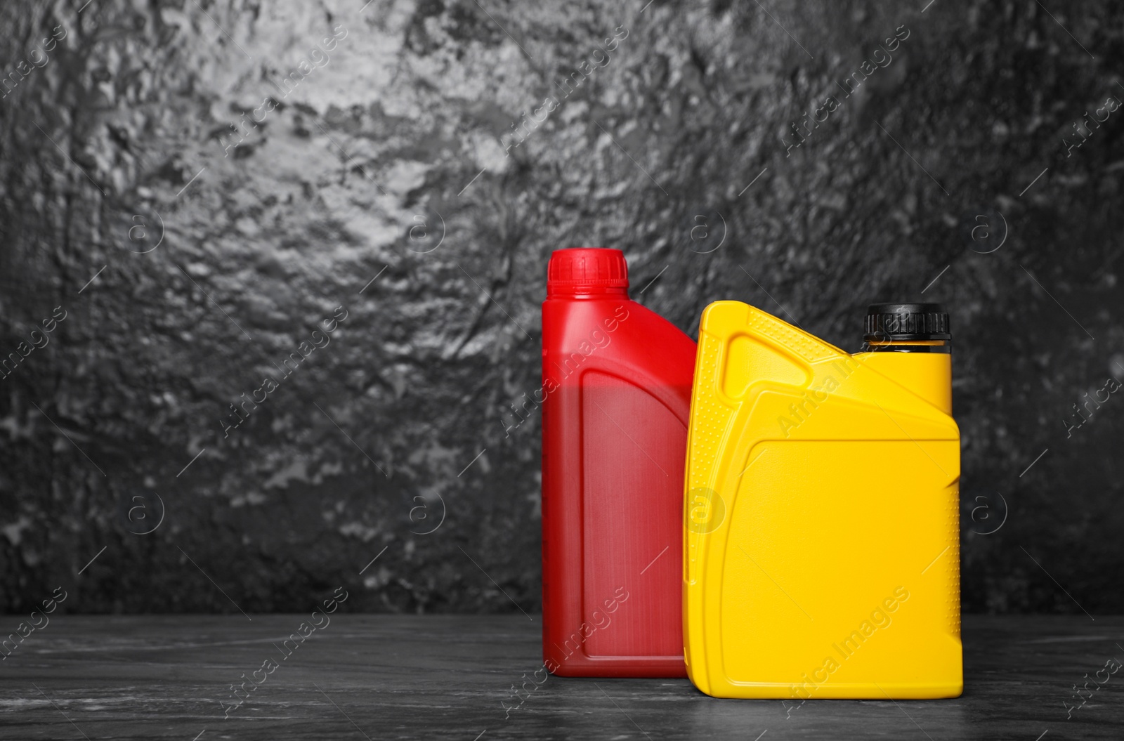 Photo of Motor oil in different canisters on black table near dark wall, space for text