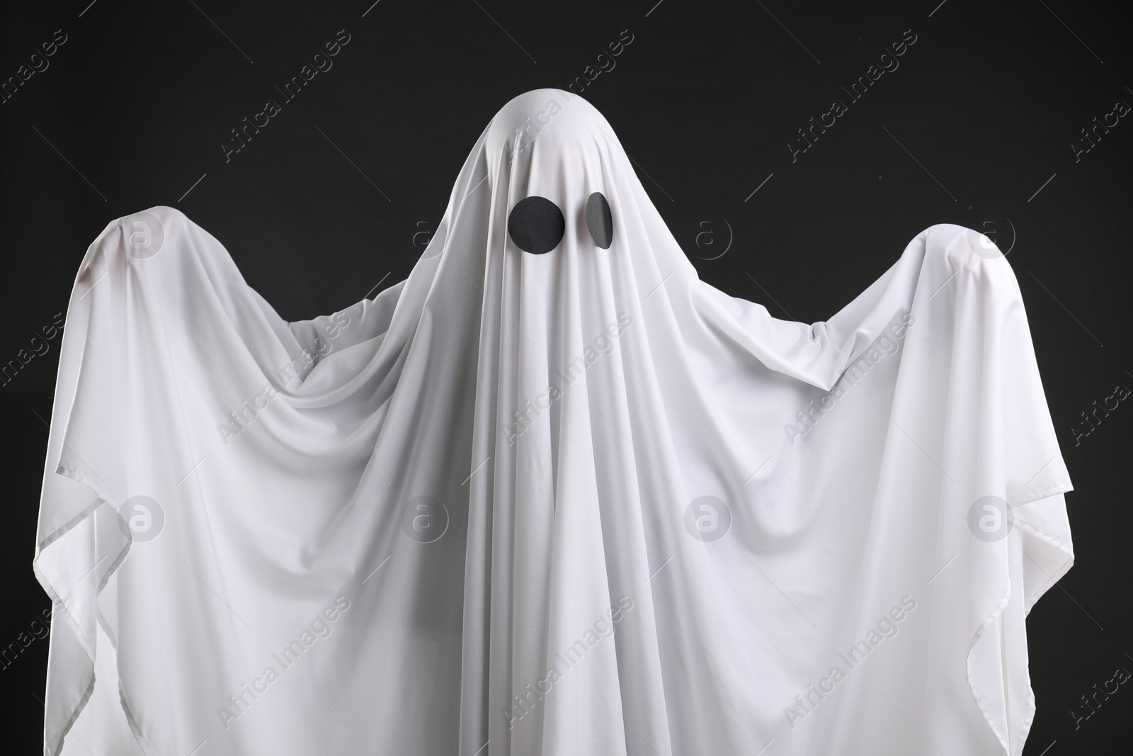 Photo of Creepy ghost. Person covered with white sheet on black background