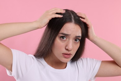 Emotional woman suffering from dandruff problem on pink background