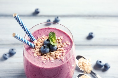 Tasty blueberry smoothie with oatmeal and berries in glass on table, closeup