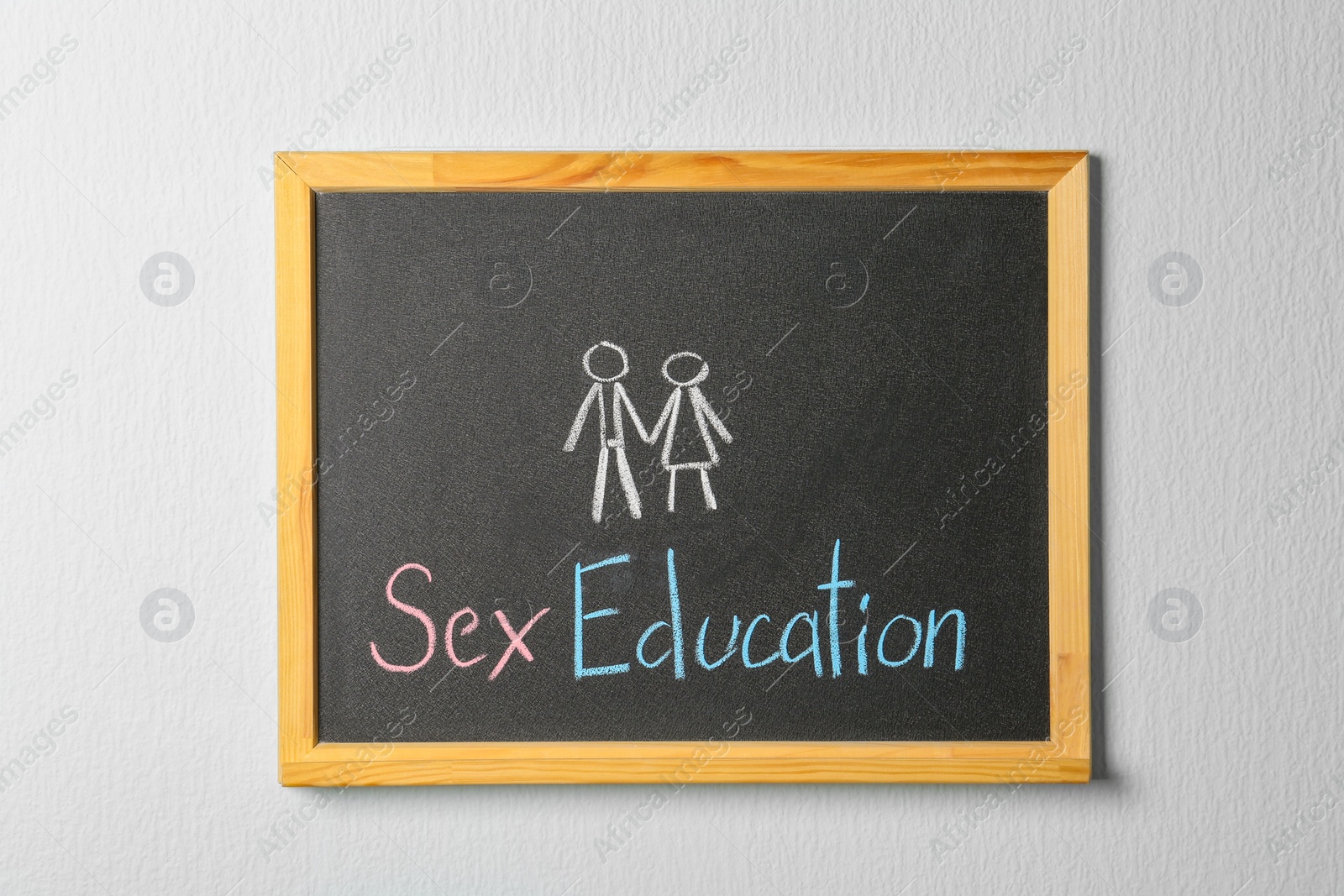 Photo of Small blackboard with written phrase "SEX EDUCATION" on white wall