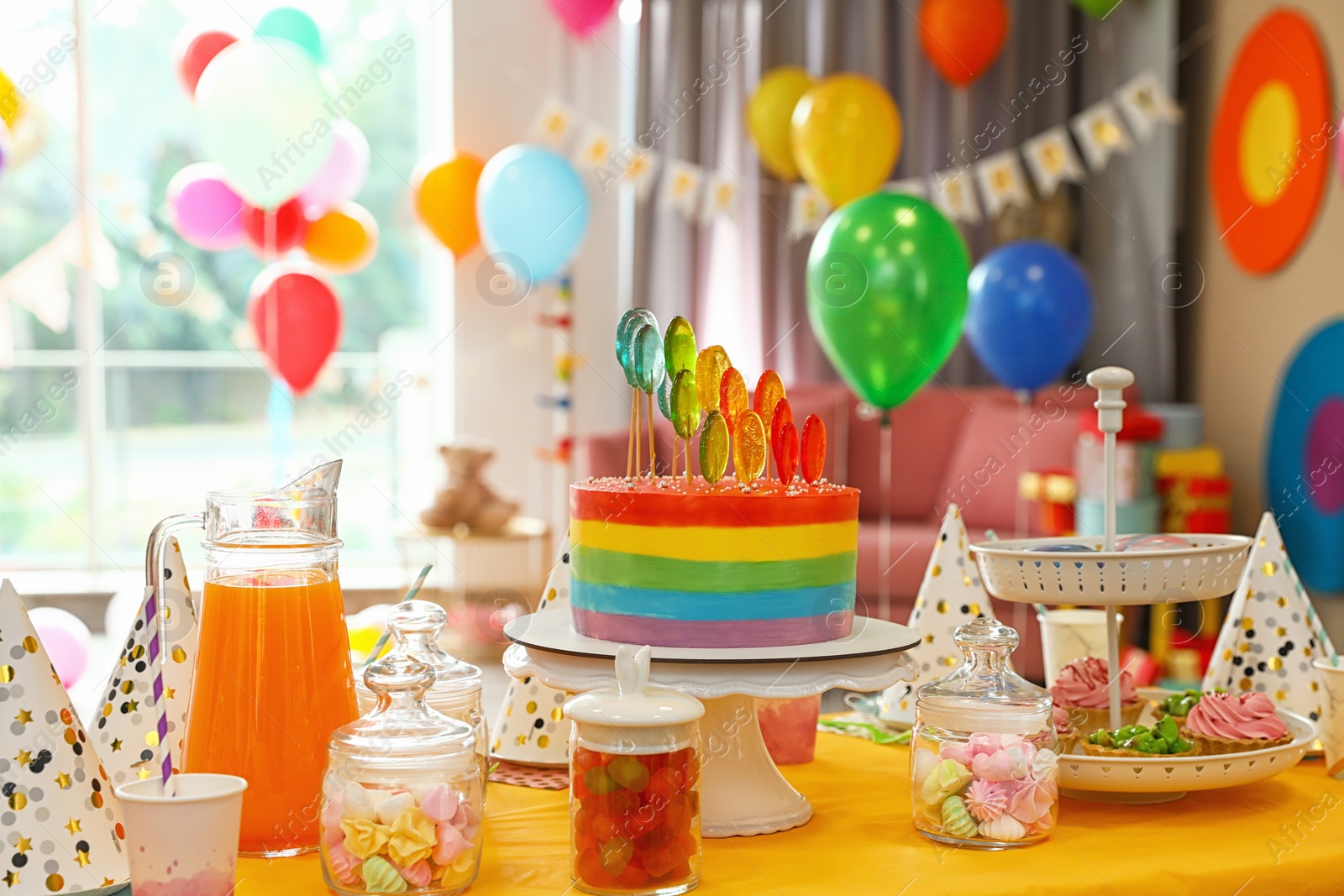 Photo of Bright birthday cake and other treats on table in decorated room