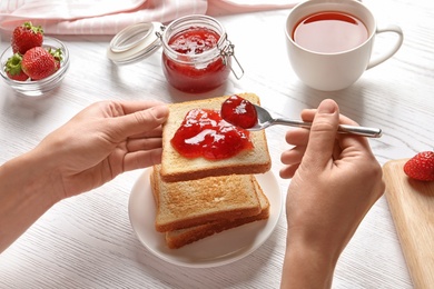 Photo of Woman spreading strawberry jam on toast bread over table