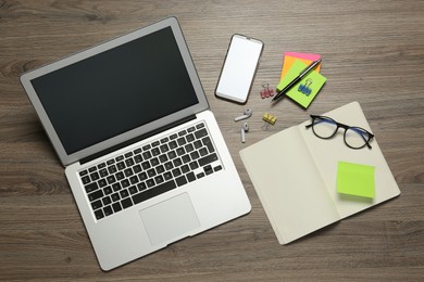 Photo of Modern laptop, smartphone and office stationery on wooden table, flat lay. Distance learning