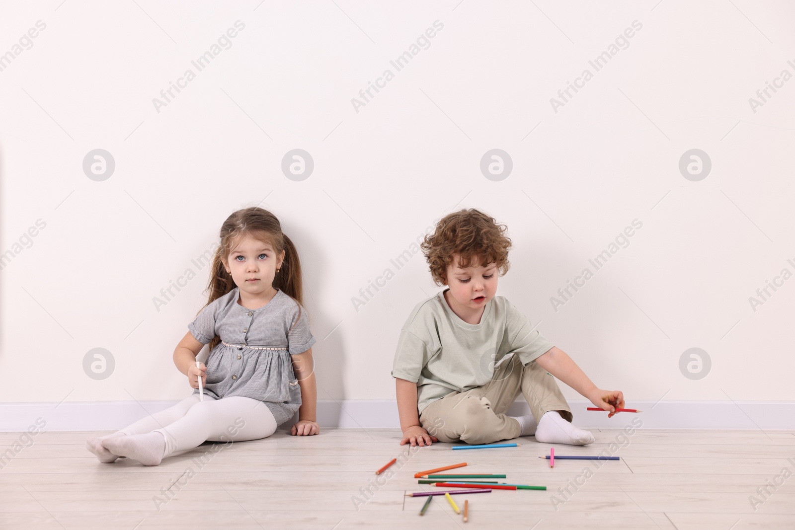 Photo of Cute little children with colorful pencils near white wall indoors