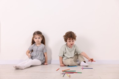 Cute little children with colorful pencils near white wall indoors