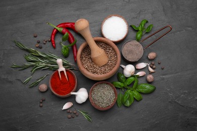 Mortar with pestle and different spices on black table, flat lay