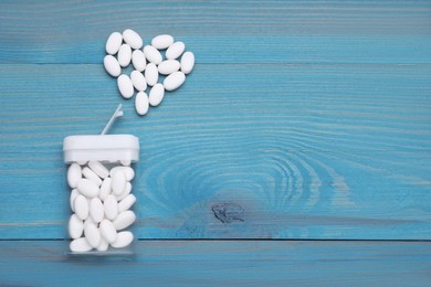 Heart made of tasty dragee candies and container on blue wooden table, flat lay. Space for text