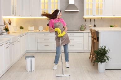 Photo of Enjoying cleaning. Happy woman in headphones dancing with mop in kitchen