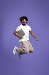 Photo of Happy man with laptop jumping on purple background