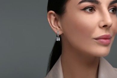 Beautiful young woman with elegant earrings on dark grey background, closeup