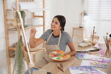 Photo of Young woman drawing on easel with brush, closeup