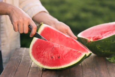 Man cutting tasty ripe watermelon at wooden table outdoors, closeup