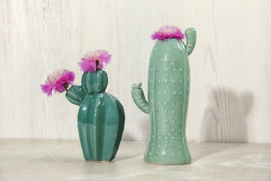 Photo of Trendy cactus shaped ceramic vases with flowers on table against wooden background