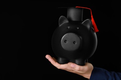 Photo of Man holding piggy bank and graduation cap against black background, closeup with space for text. Scholarship concept
