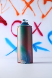 One spray paint can near white wall with different drawn symbols