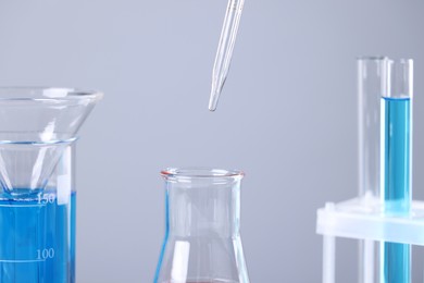 Pipette over glass flask on grey background, closeup