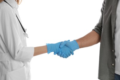 Doctor and patient in protective gloves shaking hands on white background, closeup