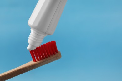 Photo of Squeezing toothpaste onto brush against light blue background, closeup. Space for text