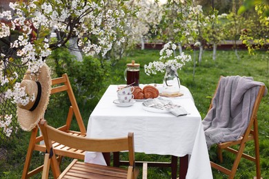 Photo of Stylish table setting with beautiful spring flowers, tea and croissants in garden