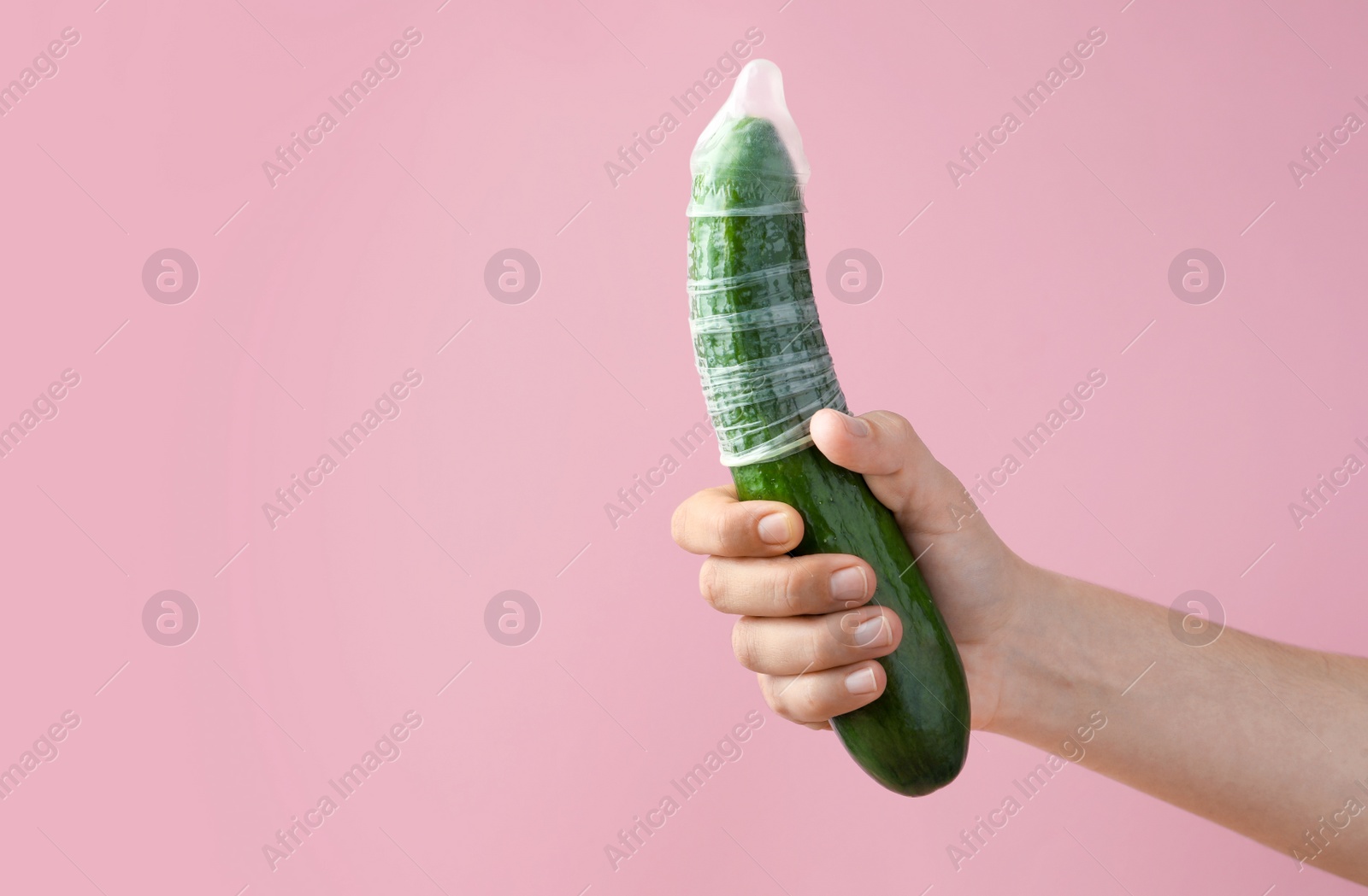 Photo of Woman holding cucumber in condom on pink background, closeup and space for text. Safe sex concept