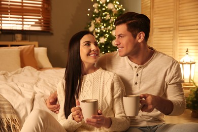Happy couple with cups in festively decorated bedroom. Christmas celebration