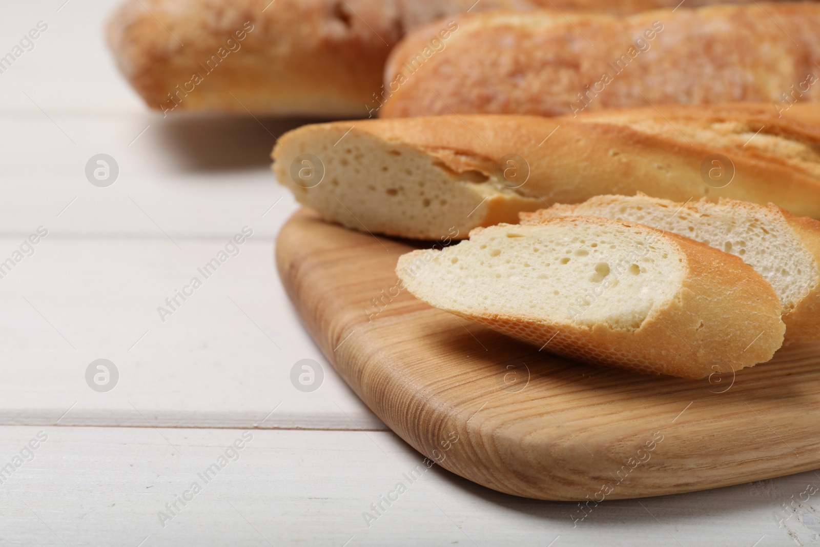 Photo of Cut tasty baguette on white wooden table, closeup. Space for text