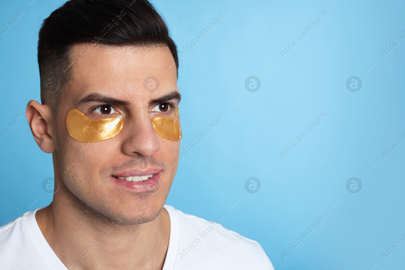 Photo of Man with golden under eye patches on light blue background. Space for text