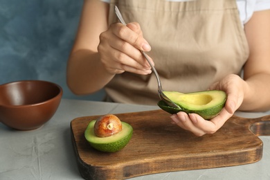 Woman scooping ripe avocado with spoon at table