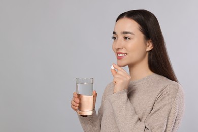 Photo of Happy woman with glass of water and pill on gray background, space for text