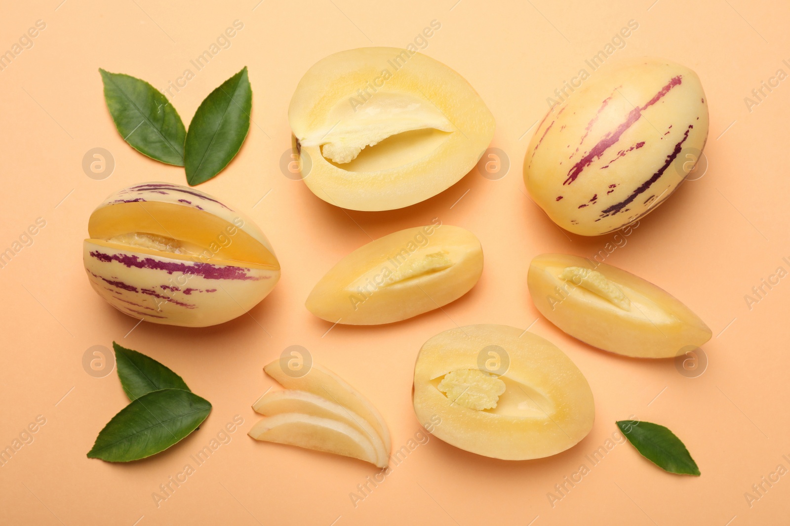 Photo of Whole and cut pepino melons with green leaves on beige background, flat lay