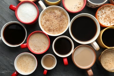 Many cups of different coffees on slate table, flat lay